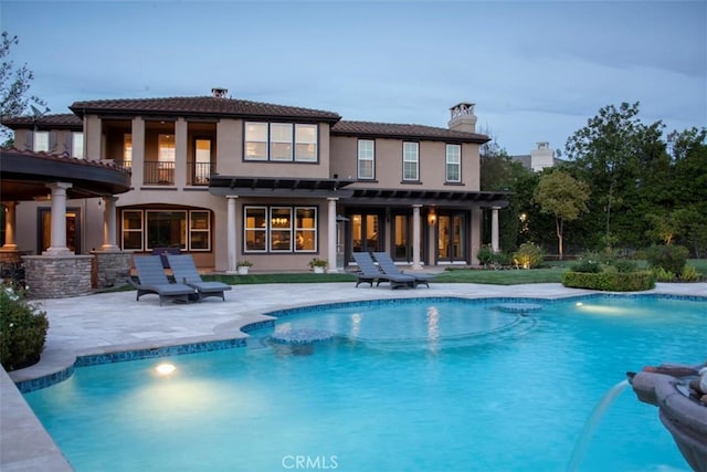 rear view of house with a chimney, an outdoor pool, a balcony, and a patio