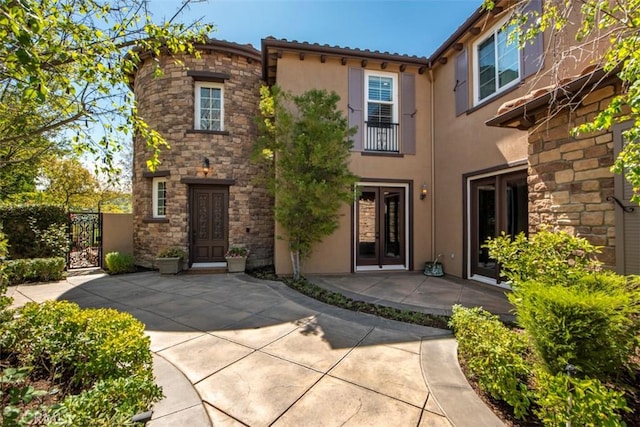 view of front of property with a gate, french doors, stucco siding, and stone siding
