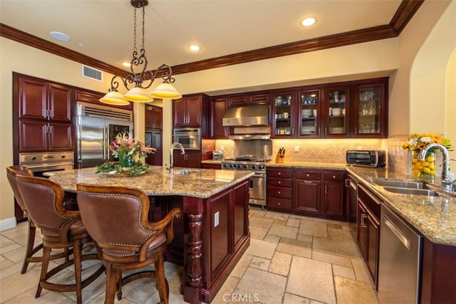 kitchen with a sink, premium appliances, under cabinet range hood, visible vents, and reddish brown cabinets