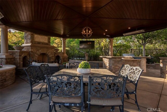 view of patio / terrace featuring an outdoor stone fireplace, exterior kitchen, outdoor dining space, a gazebo, and fence