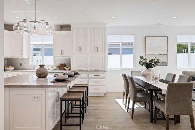 kitchen featuring white cabinets, a center island, light wood-style floors, decorative backsplash, and a breakfast bar area