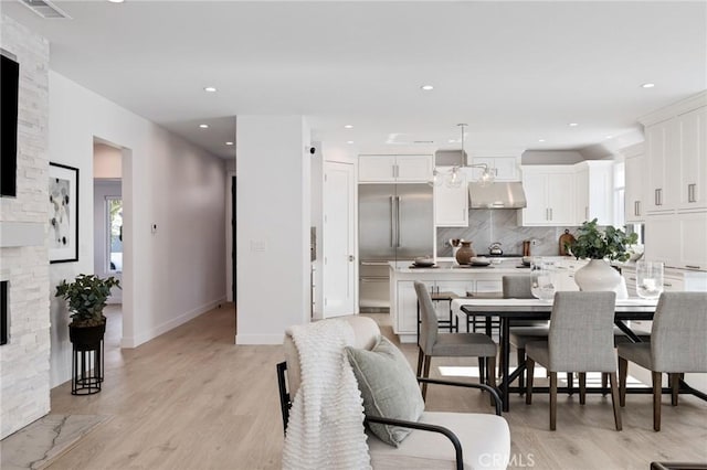 dining room with recessed lighting, light wood finished floors, a stone fireplace, visible vents, and baseboards