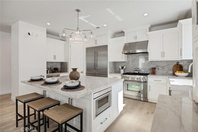 kitchen featuring light stone counters, built in appliances, light wood-style flooring, white cabinets, and under cabinet range hood