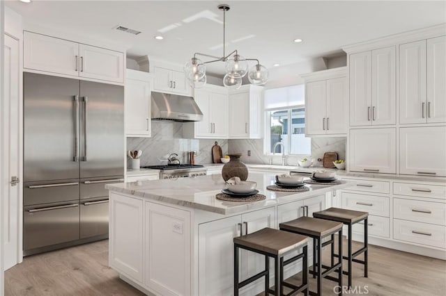 kitchen featuring white cabinets, under cabinet range hood, light wood-style floors, a kitchen island, and stainless steel built in refrigerator