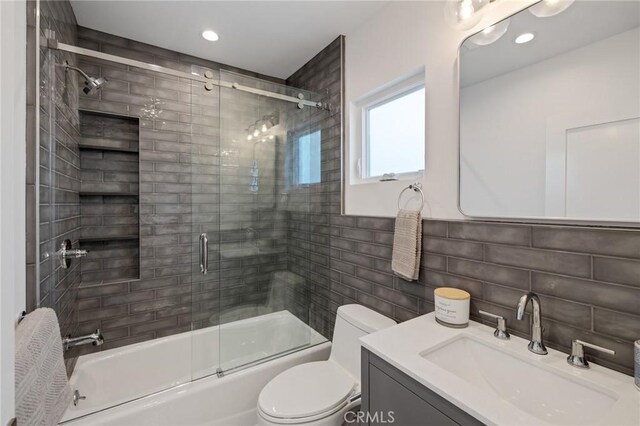 full bathroom featuring combined bath / shower with glass door, toilet, vanity, tile walls, and tasteful backsplash