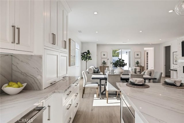 kitchen featuring light stone counters, light wood-style flooring, open floor plan, and white cabinetry