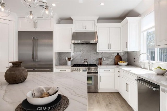 kitchen featuring high end appliances, under cabinet range hood, a sink, and white cabinetry