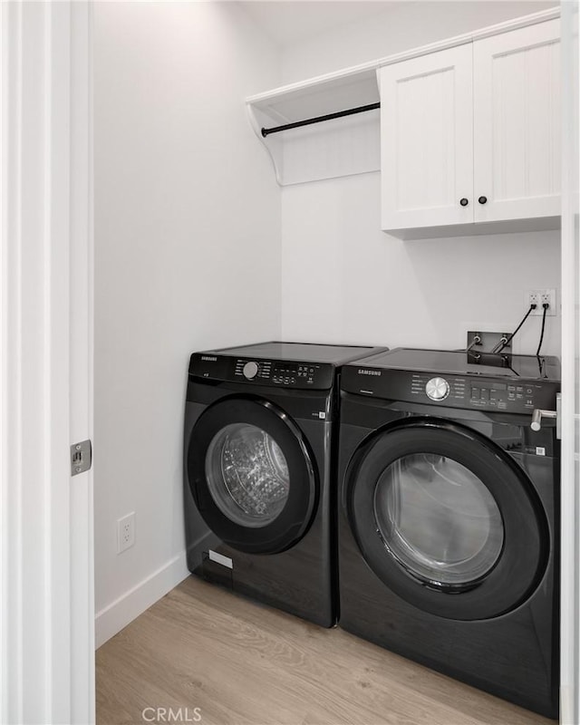 clothes washing area featuring cabinet space, light wood-type flooring, baseboards, and separate washer and dryer
