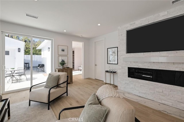 living area with recessed lighting, light wood-style floors, a stone fireplace, and visible vents