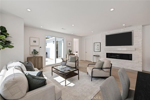 living room with recessed lighting, light wood-style flooring, and a stone fireplace