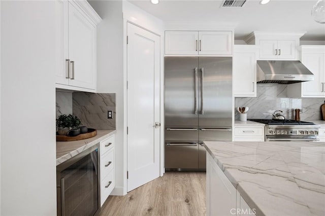 kitchen featuring white cabinets, premium appliances, beverage cooler, and under cabinet range hood