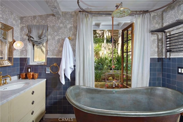 full bathroom featuring wallpapered walls, a wainscoted wall, and tile walls