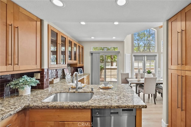 kitchen with light stone countertops, decorative backsplash, dishwasher, and a sink
