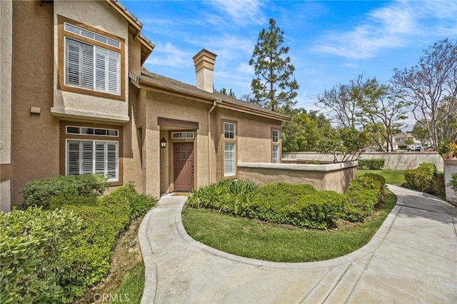 view of front of house with a chimney, fence, and stucco siding