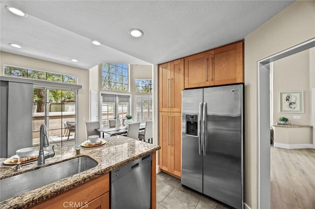 kitchen featuring brown cabinetry, stone counters, a sink, and appliances with stainless steel finishes