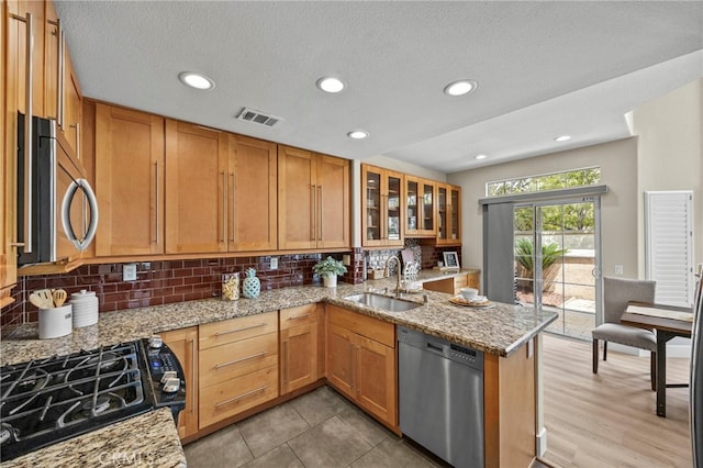 kitchen featuring tasteful backsplash, appliances with stainless steel finishes, light stone counters, and a sink