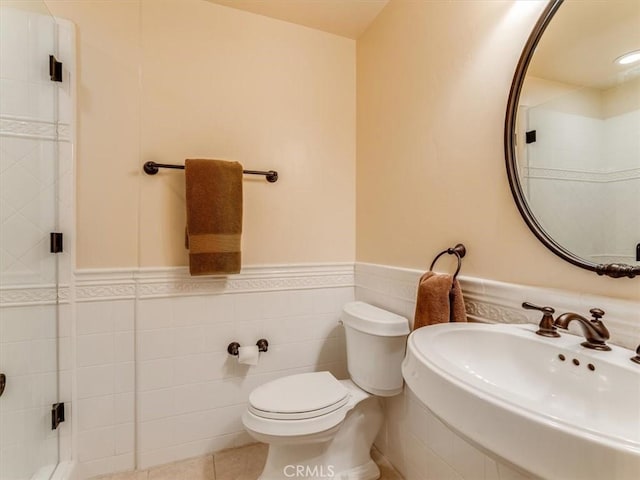 bathroom with tile patterned floors, a wainscoted wall, toilet, a sink, and tile walls