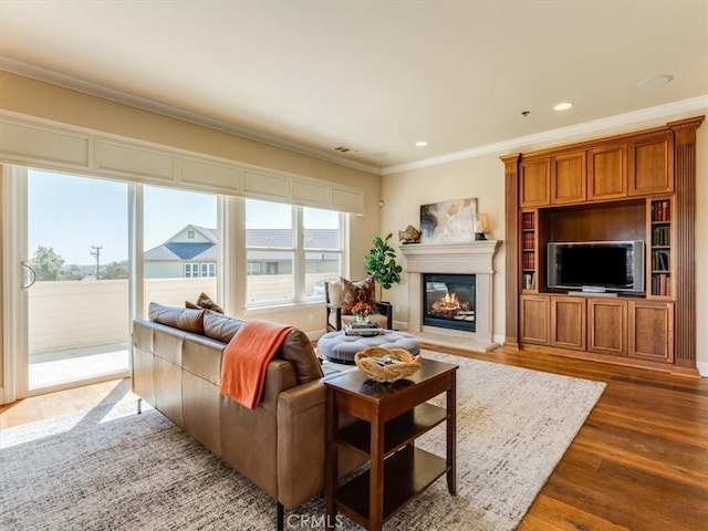 living area featuring recessed lighting, a glass covered fireplace, wood finished floors, and ornamental molding