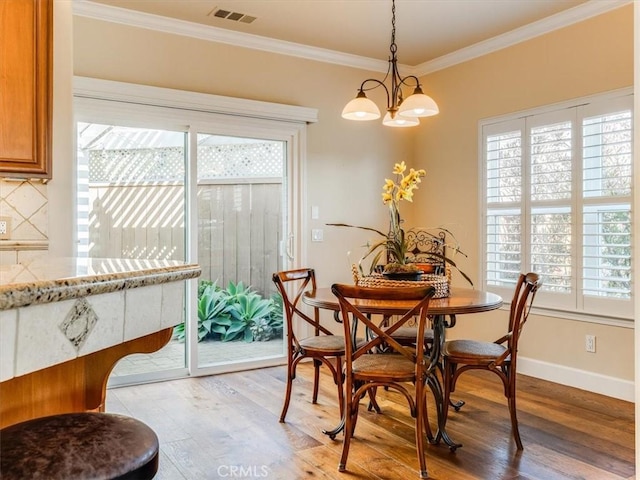 dining room featuring light wood-style floors, visible vents, baseboards, and ornamental molding