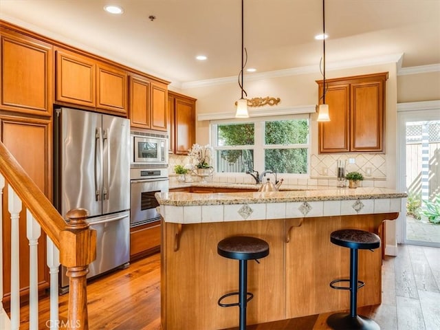 kitchen with brown cabinetry, ornamental molding, a breakfast bar, backsplash, and appliances with stainless steel finishes