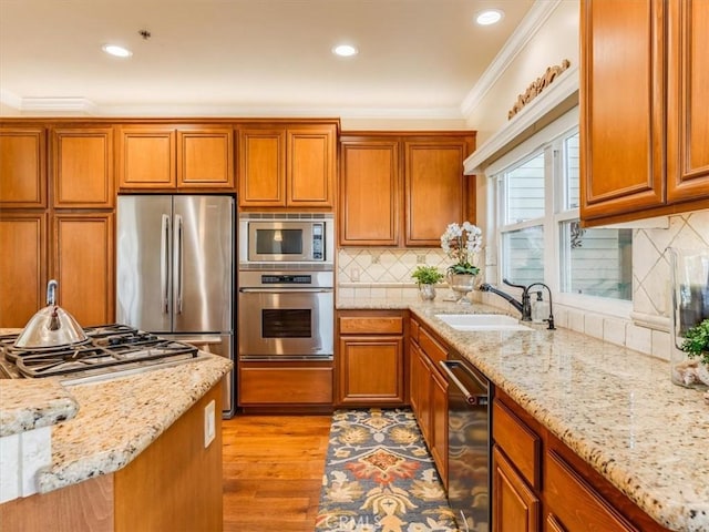 kitchen featuring stainless steel appliances, light wood-style flooring, a sink, brown cabinets, and ornamental molding