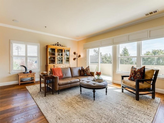living room with hardwood / wood-style floors, visible vents, baseboards, and ornamental molding