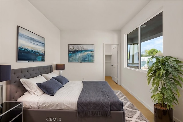 bedroom featuring light wood-type flooring, baseboards, and a spacious closet