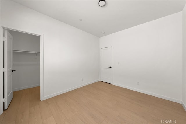 unfurnished bedroom featuring a spacious closet, baseboards, a closet, and light wood-style floors