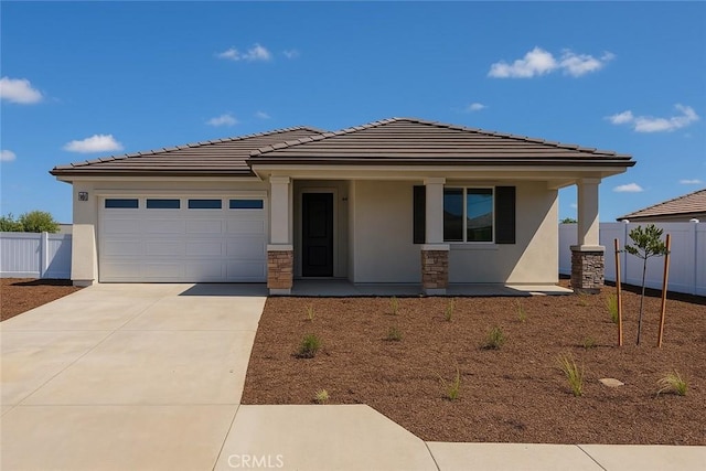 prairie-style home featuring a porch, fence, an attached garage, and driveway