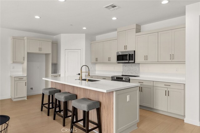 kitchen with visible vents, a kitchen island with sink, a sink, stainless steel appliances, and a breakfast bar area