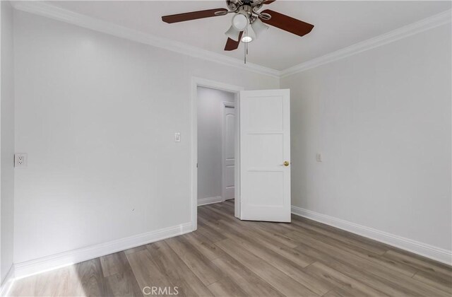 spare room with ornamental molding, baseboards, light wood-type flooring, and a ceiling fan