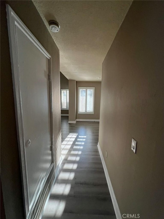 hallway with baseboards, wood finished floors, and a textured ceiling