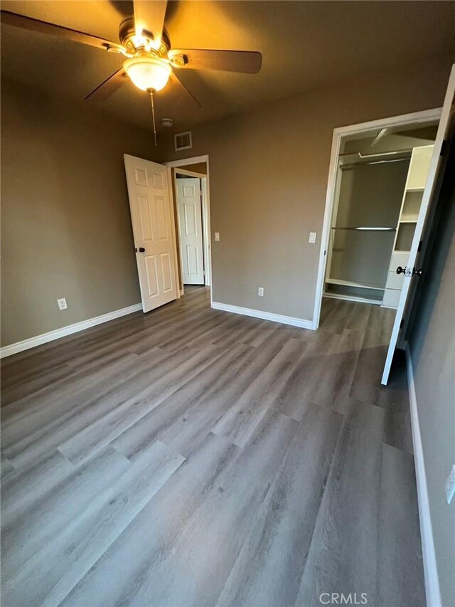 unfurnished bedroom with a spacious closet, visible vents, baseboards, and dark wood-style floors