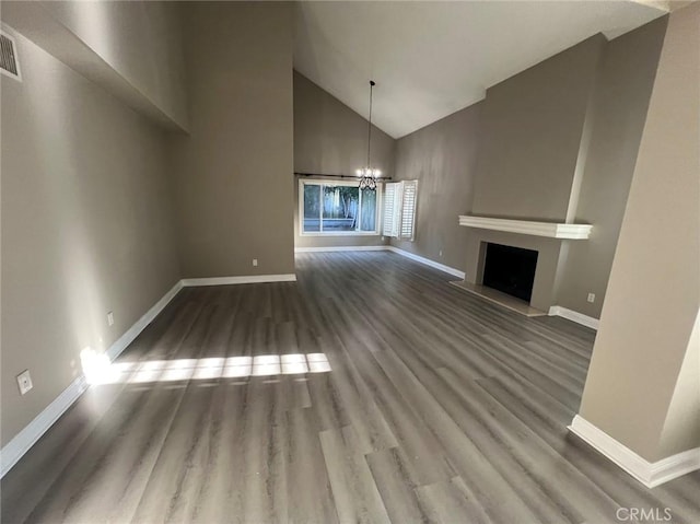 unfurnished living room with a fireplace with raised hearth, a notable chandelier, baseboards, and wood finished floors