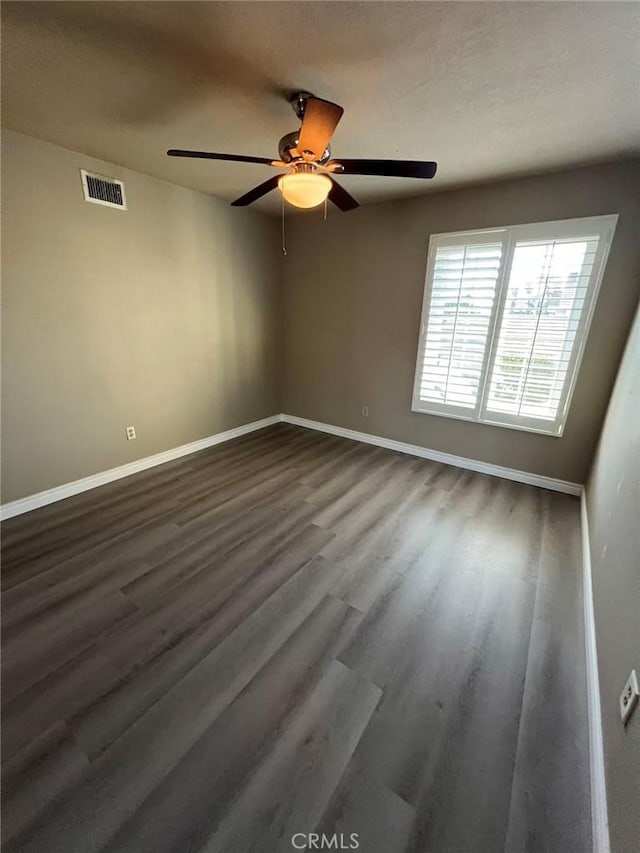 spare room with dark wood-type flooring, visible vents, baseboards, and a ceiling fan