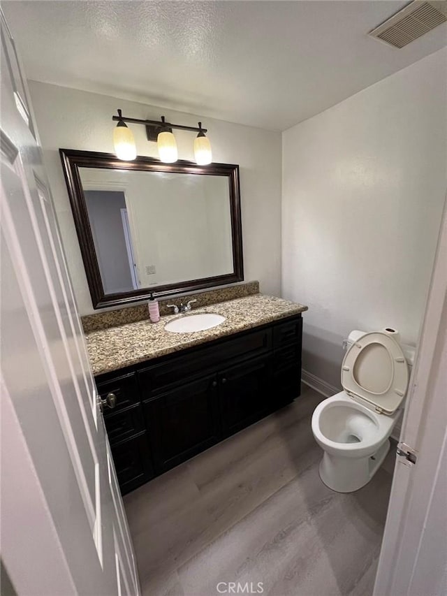 bathroom with visible vents, toilet, vanity, and wood finished floors