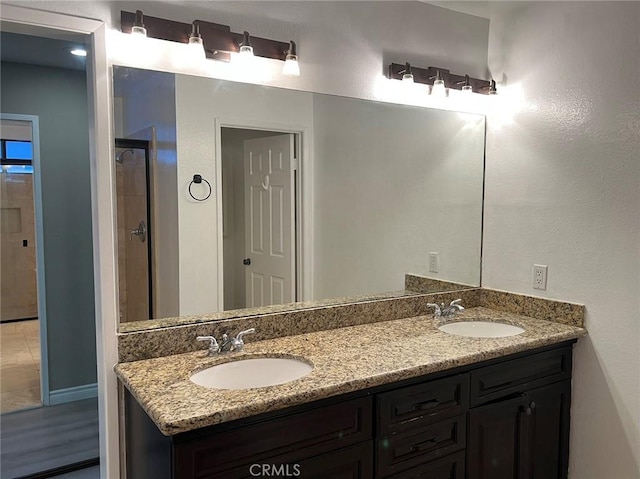 full bathroom featuring walk in shower, double vanity, baseboards, and a sink