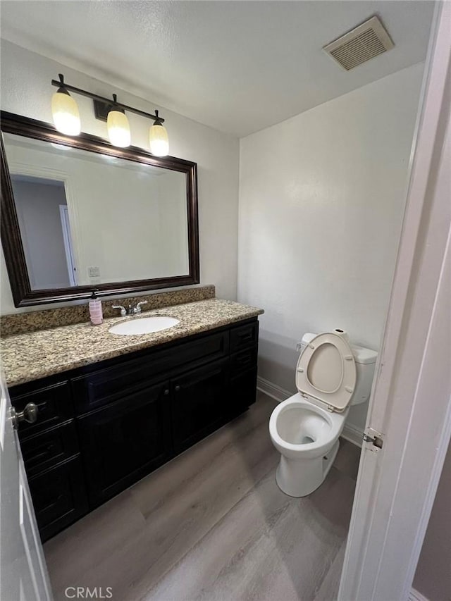 bathroom featuring vanity, baseboards, toilet, visible vents, and wood finished floors