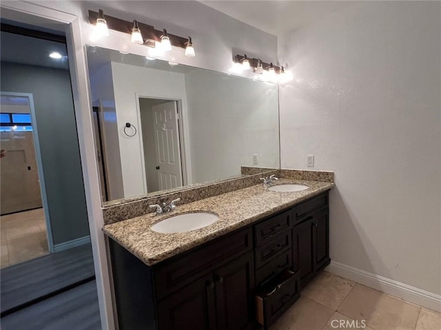 bathroom with double vanity, a sink, tile patterned flooring, and baseboards