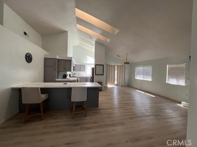 kitchen with wood finished floors, refrigerator, a breakfast bar area, high vaulted ceiling, and a peninsula