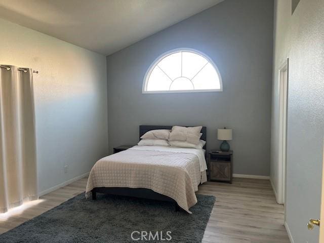 bedroom with baseboards, light wood-style flooring, and vaulted ceiling