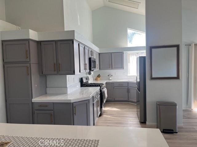 kitchen with stainless steel appliances, light wood-style floors, gray cabinets, high vaulted ceiling, and light countertops