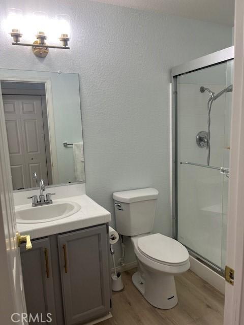 full bathroom with wood finished floors, a shower stall, toilet, and vanity