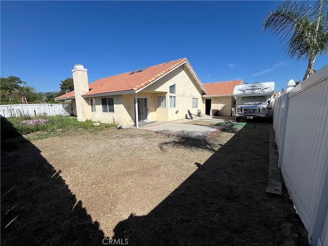 rear view of property featuring a fenced backyard, stucco siding, a tiled roof, and a chimney