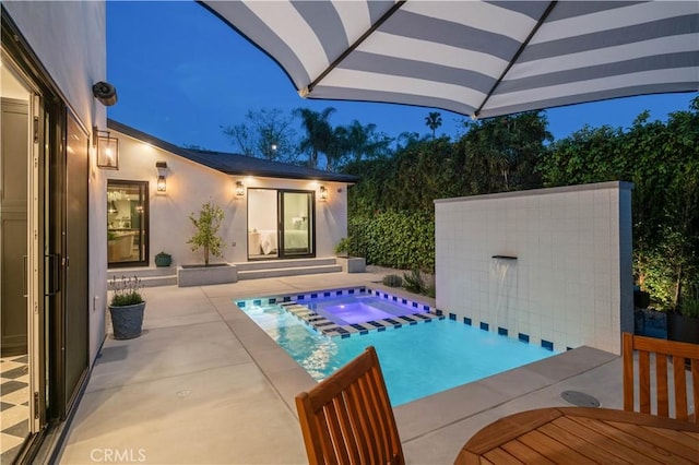 pool at night with a patio and an in ground hot tub