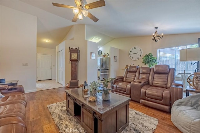 living area with baseboards, ceiling fan with notable chandelier, lofted ceiling, and light wood-type flooring