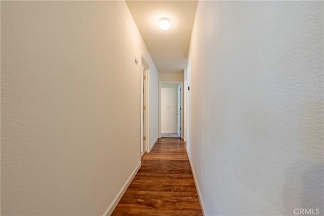 hallway with baseboards, a textured wall, and dark wood-type flooring