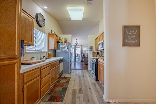 kitchen featuring a sink, light wood-style floors, tile counters, stainless steel appliances, and a wealth of natural light