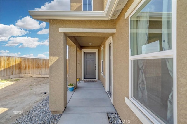 entrance to property with a patio area, stucco siding, and fence