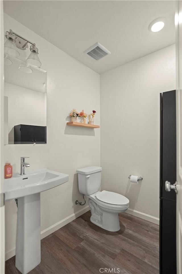 half bath with visible vents, baseboards, toilet, and wood finished floors
